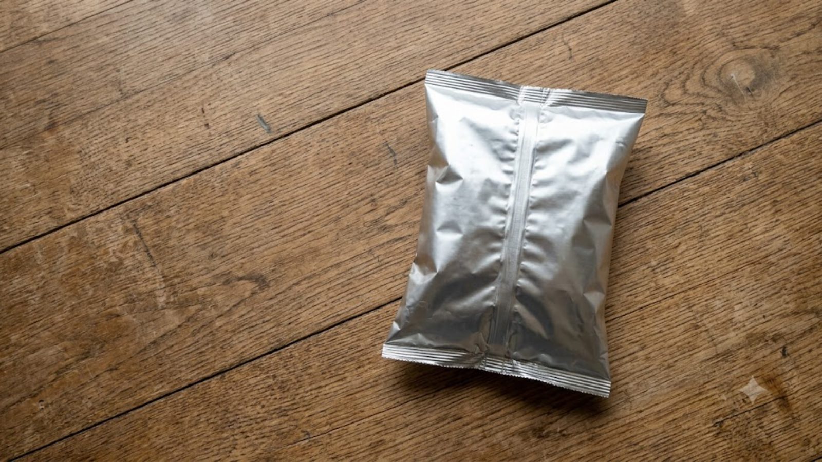 A single unbranded foil snack bag on a bare shop counter, shot from directly overhead