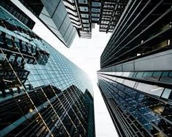 Looking straight up between glass-and-steel office towers that close in on a pale sky, their windows reflecting one another in cool light.