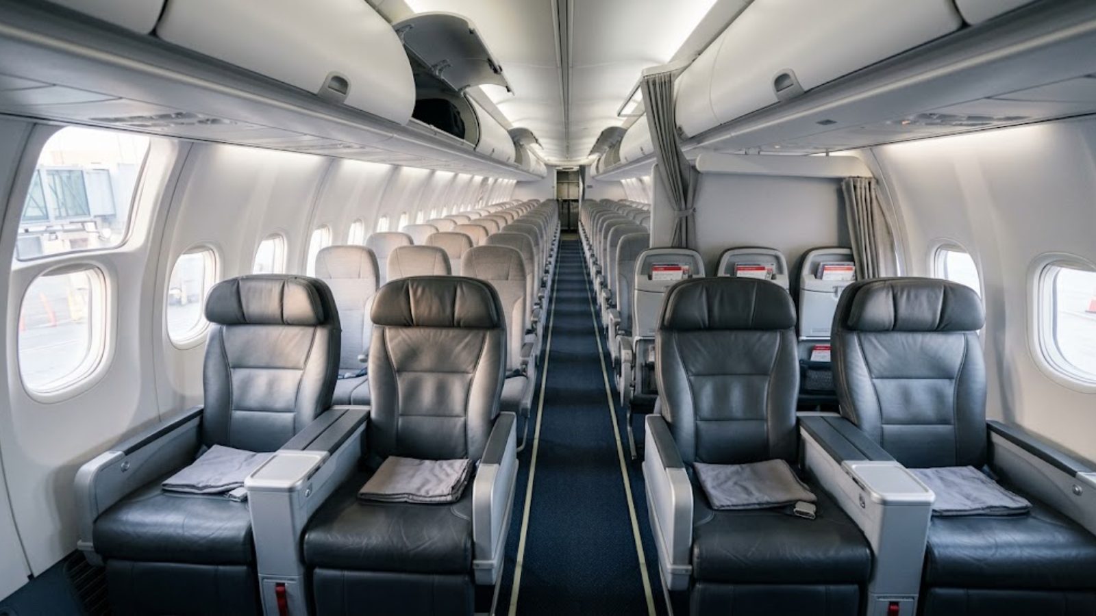 The forward cabin of a narrow-body jet with two rows of wider seats ahead of standard rows, morning light through the windows, no passengers.