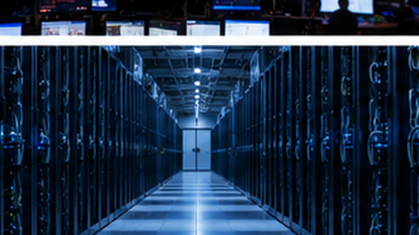 A brightly lit corridor between two long rows of server racks behind glass, with a bank of monitors visible above.