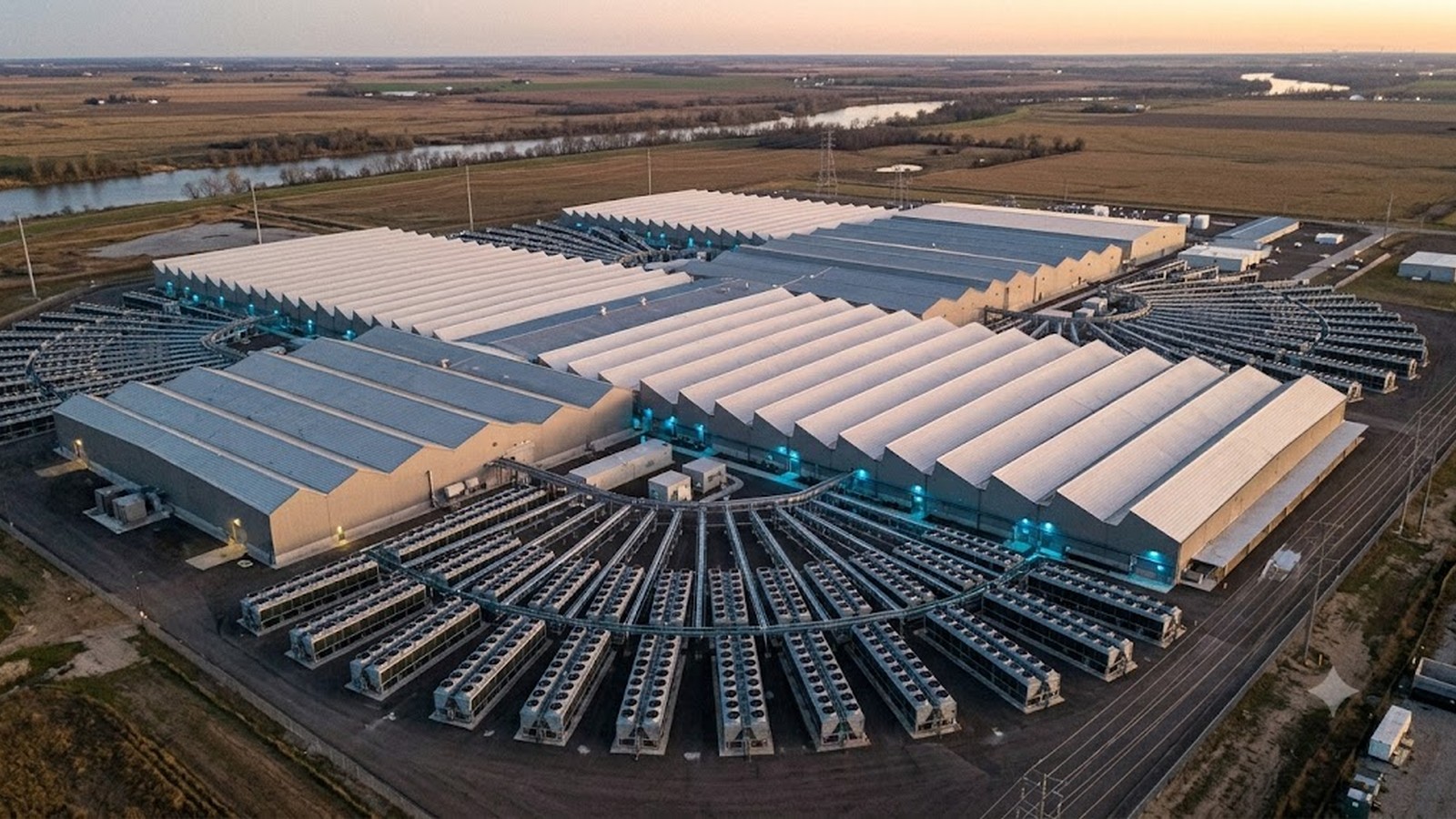 An aerial view of a sprawling data-center campus at dusk, cooling units across the roofs.